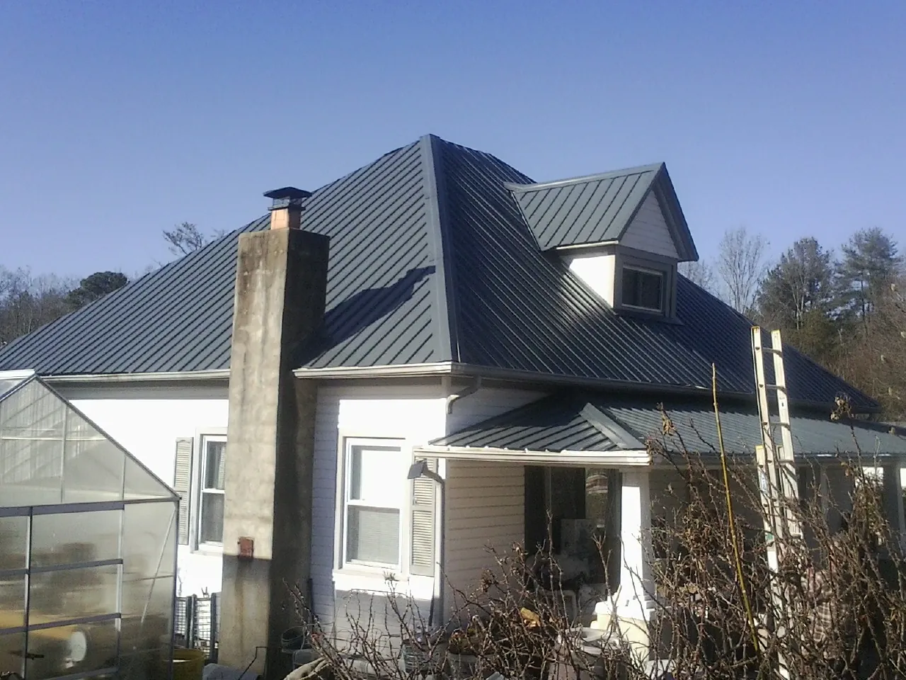 Dark blue standing seam metal roof on a white farmhouse with dormer — Slate & Tile Roof Repair by Roofing Brothers in Lula