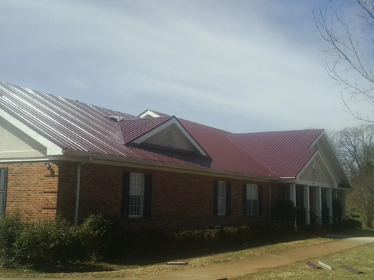 Red metal roof with gabled entries on a long brick building, from a Hail Damage Roof Repair job in Lula