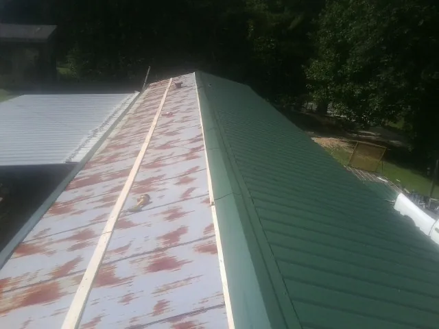 Old rusted panels beside newly installed green metal roofing — Wind Damage Roof Repair by Roofing Brothers in Lula