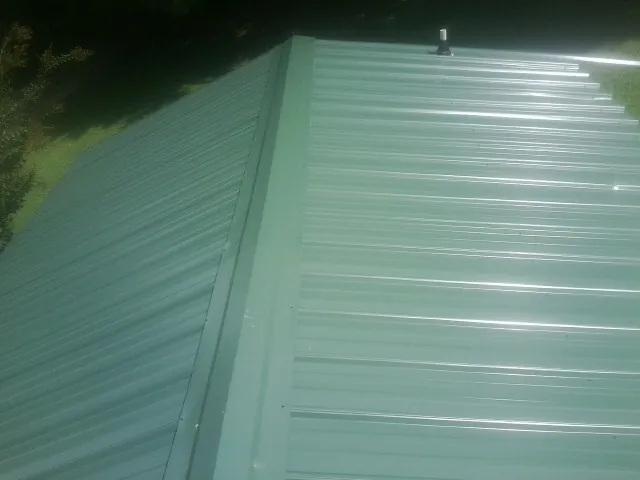 New green metal panels meeting at the ridge of a roof — Flat Roof Repair work by our crew in Lula
