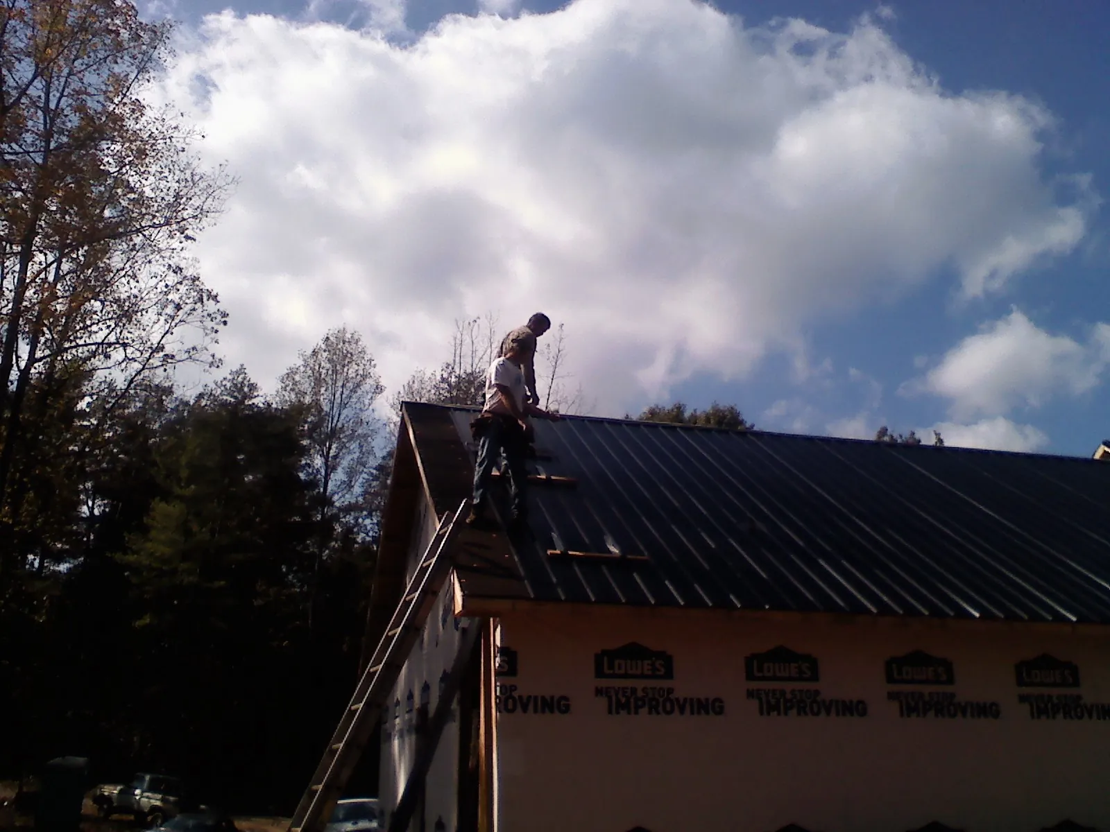 Roofer fastening dark metal panels high against a cloudy sky, from a Roof Inspection job in Lula