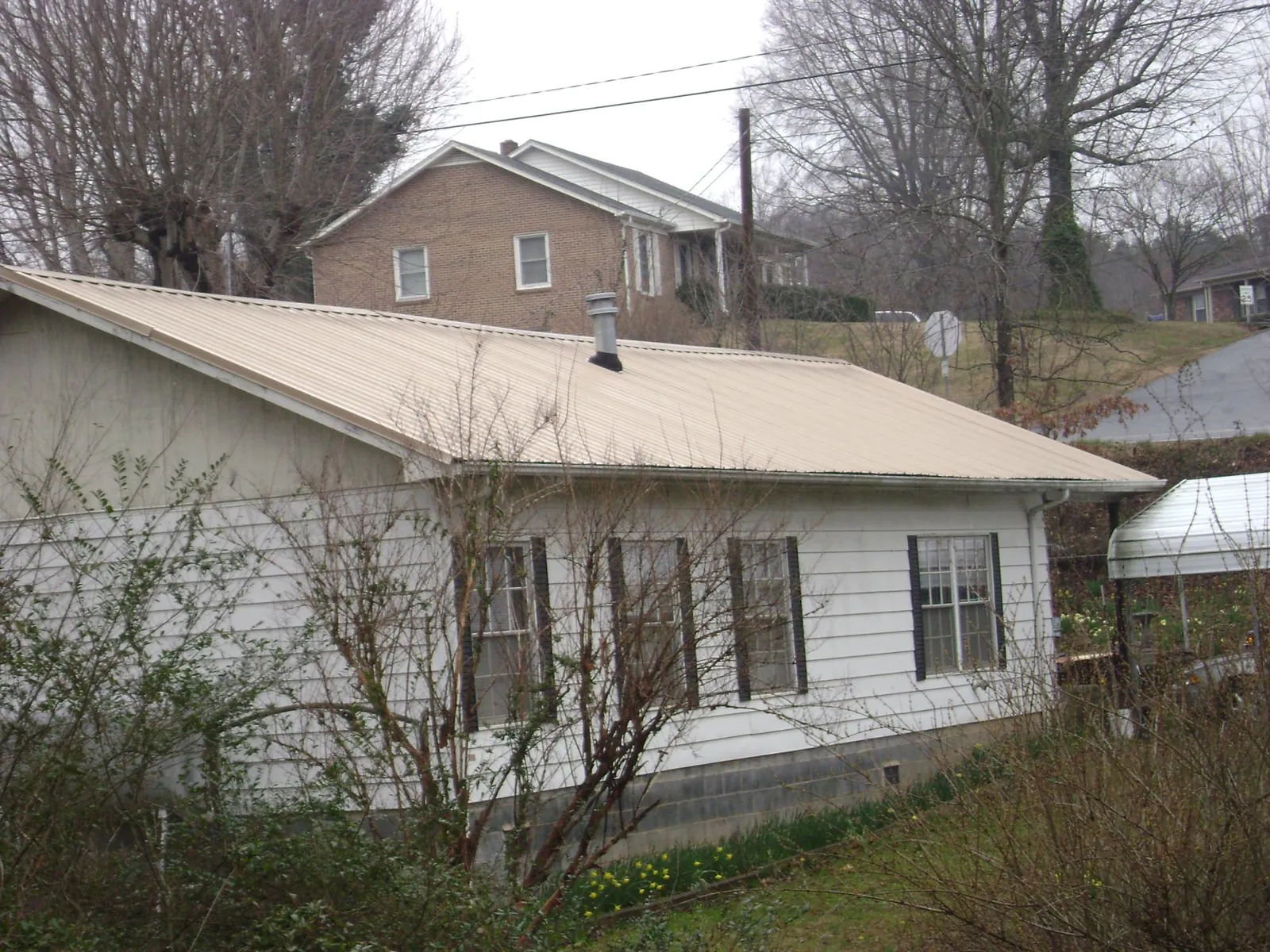 Tan metal roof on a white sided house set into a hillside — Commercial Roofing by Roofing Brothers in Lula