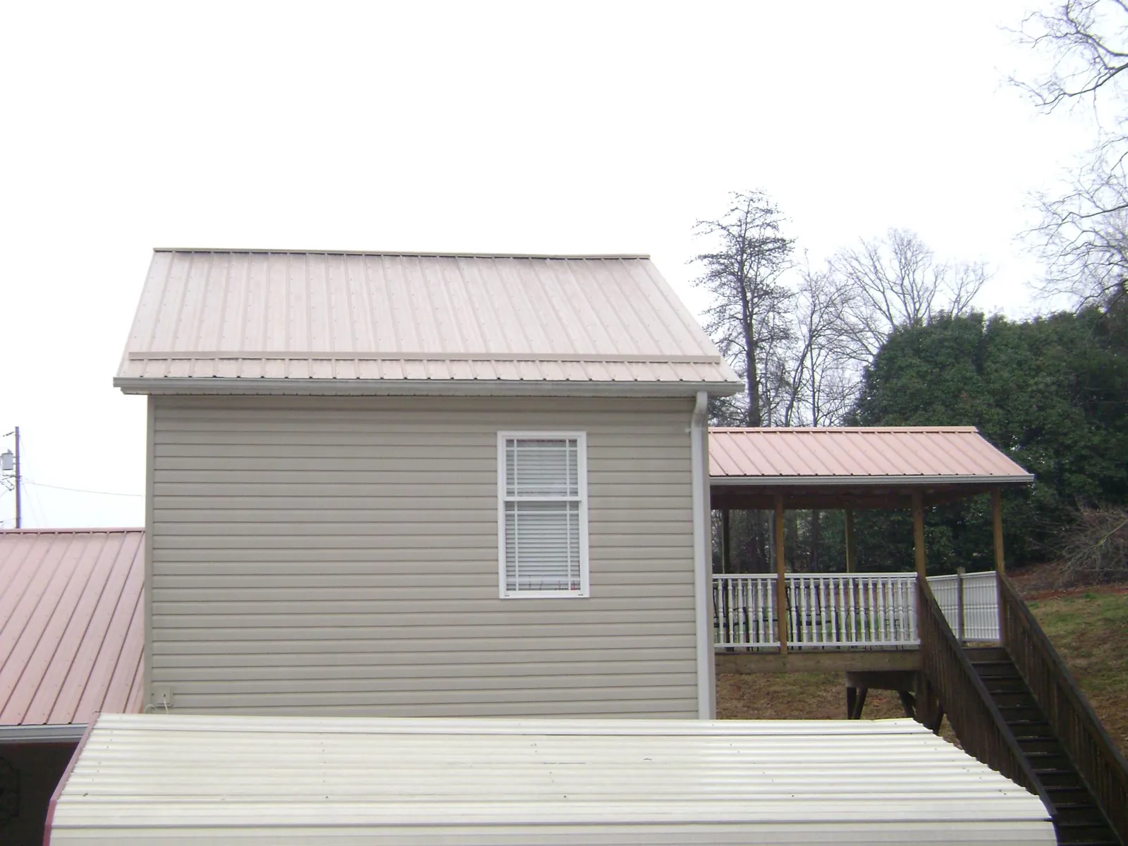 Tan metal roofs on a two story addition and attached porch, from a Roof Replacement job in Lula